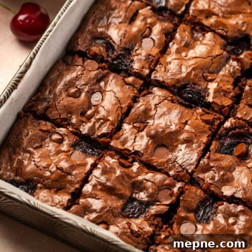 A pan of cherry chocolate brownies sitting on a table next to a bowl of cherries.