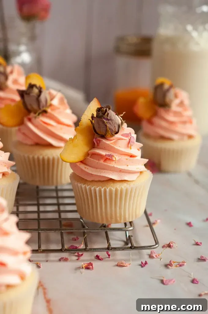 Peach rose flavored cupcakes with a peachy orange frosting swirl and a slice of fresh peach and dried rose on top for decor.