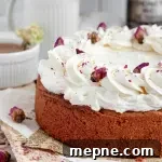 A golden honey rose cake topped with white rose buttercream and bright pink rosebuds.