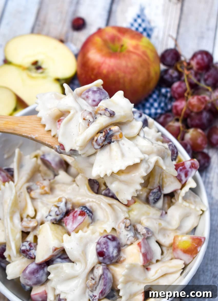 Summer Fruit and Honey Pasta Salad Recipe 7 a wooden spoon holding up a scoop of creamy pasta salad with fruit recipe