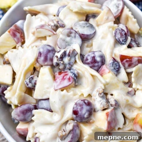 sweet pasta salad with fruit and honey in a white bowl surrounded by fresh fruits