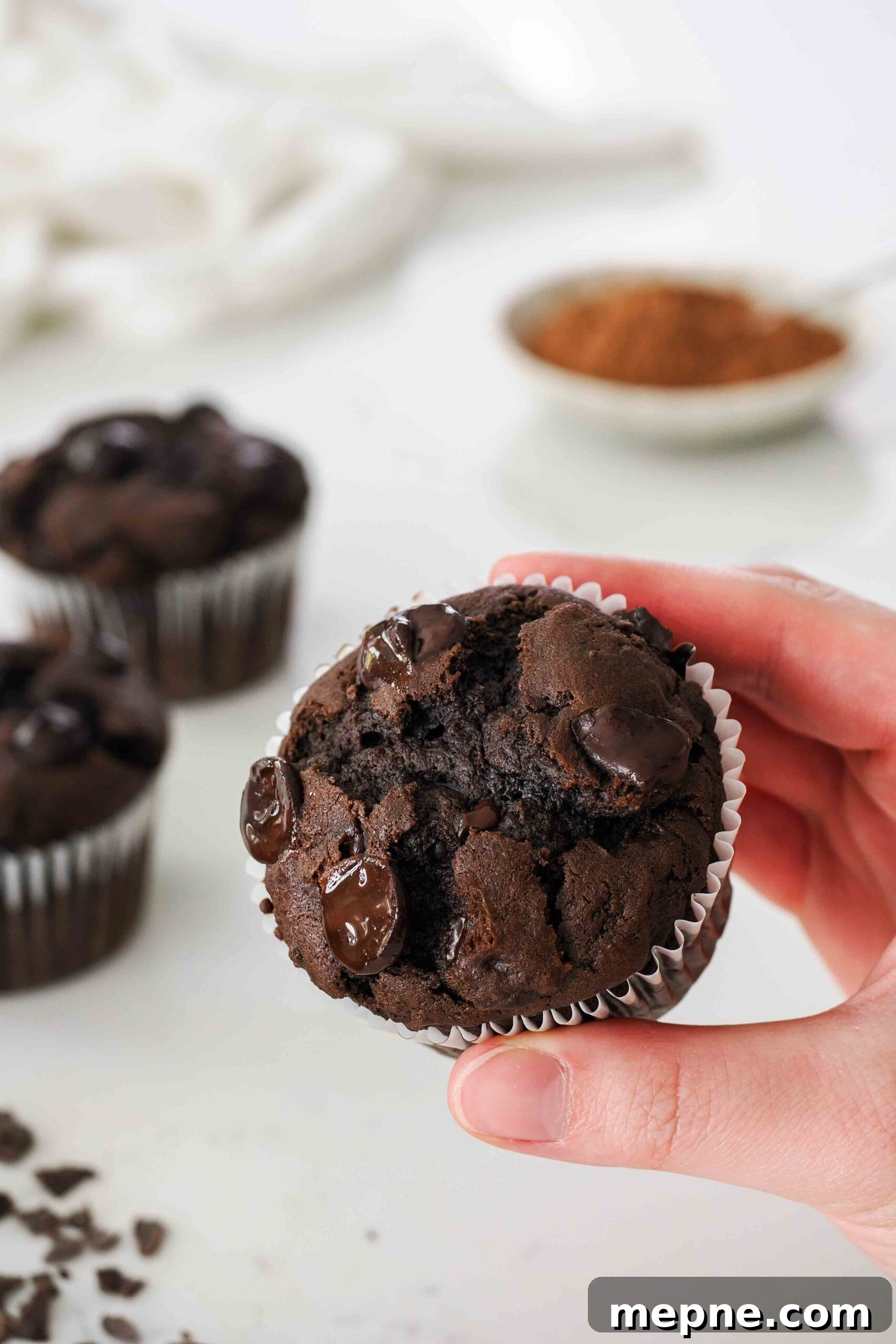 Moist and Fudgy Double Chocolate Muffins Recipe 16 A hand holds up a chocolate muffin with chocolate chips.
