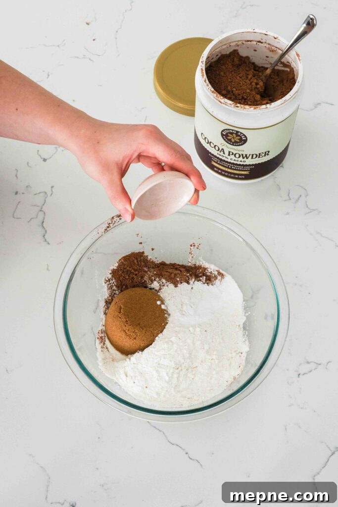 Moist and Fudgy Double Chocolate Muffins Recipe 4 A hand tips baking powder into a bowl of dry ingredients.