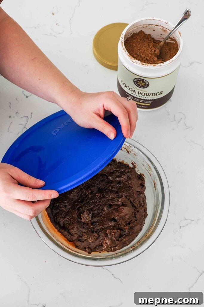 Moist and Fudgy Double Chocolate Muffins Recipe 9 Two hands bring a plastic lid over a bowl of chocolate muffin batter.