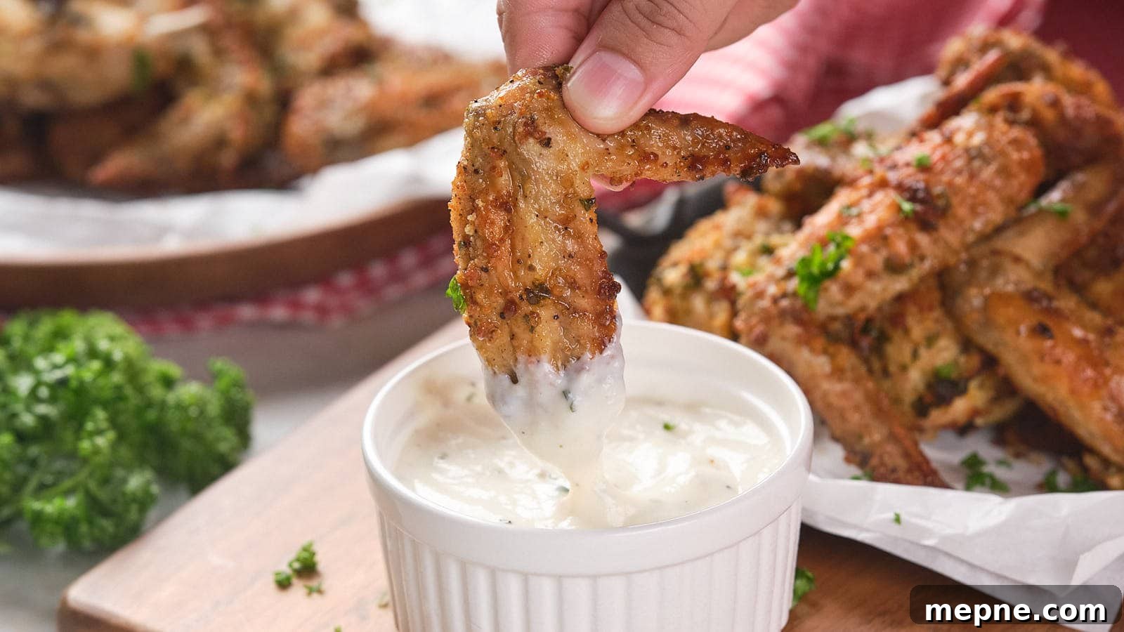 13 Low-Carb Holiday Appetizers to Impress Guests 3 A hand dips a parmesan chicken wing into a small ramekin filled with white dipping sauce.