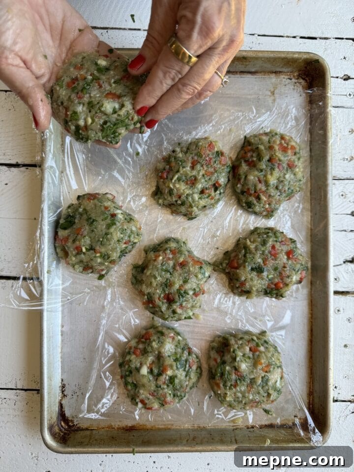 Smoky Chicken Patty Bowl: Weeknight Chicken Burger Recipe 11 two hands with red nail polish and gold ring shaping a chicken patty over a Saran Wrap lined metal tray with seven chicken patties