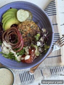 blue bowl with chicken patty avocado cucumbers red onions white dressing and greens on a blue striped napkin with fork