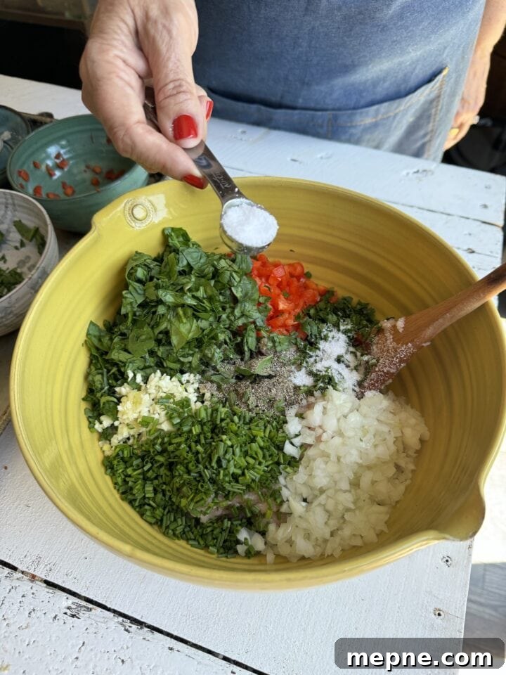 Smoky Chicken Patty Bowl: Weeknight Chicken Burger Recipe 9 adding salt to yellow bowl with spinach chives parsley garlic onions pepper red pepper and ground chicken