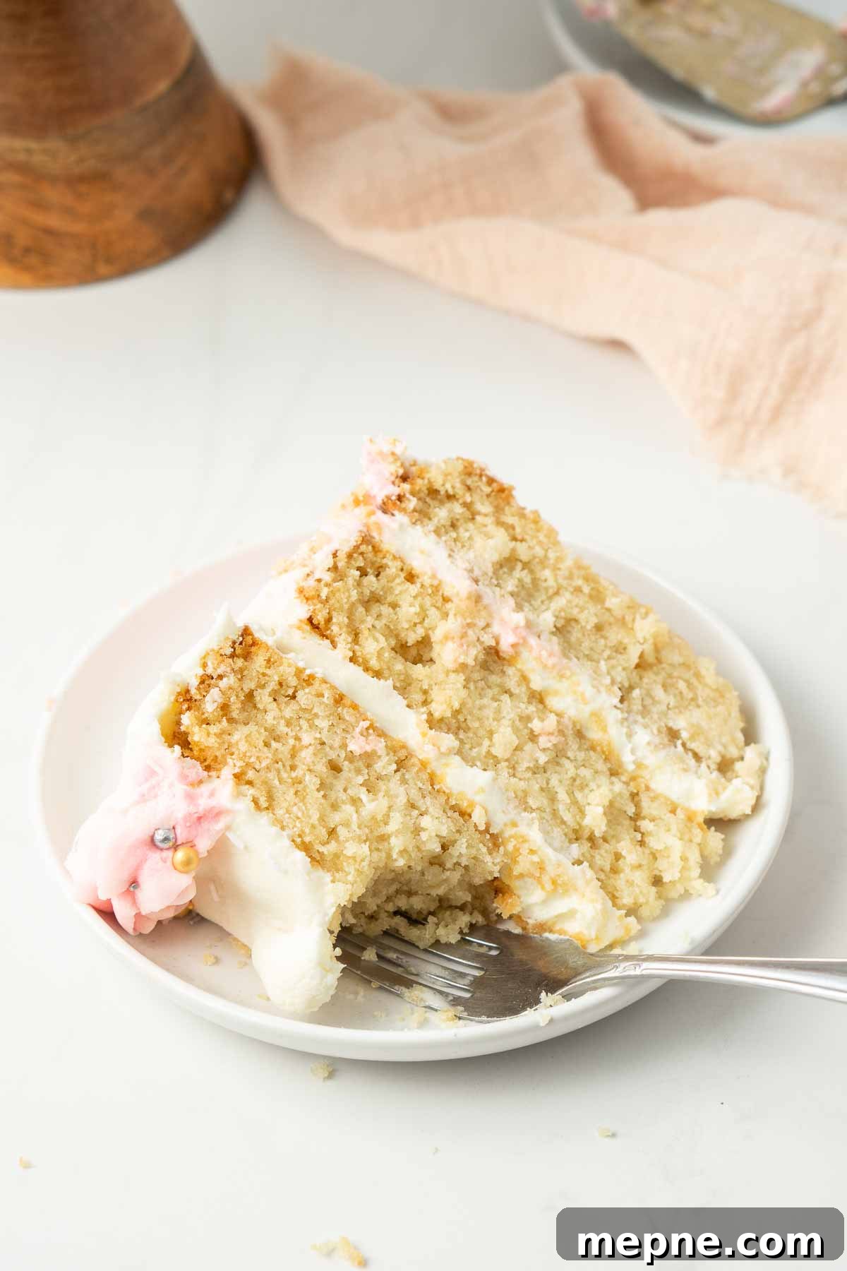 Vegan Vanilla Cake with Fluffy Frosting 12 Close up of a slice of vanilla cake on a small white place with a fork and bite taken.