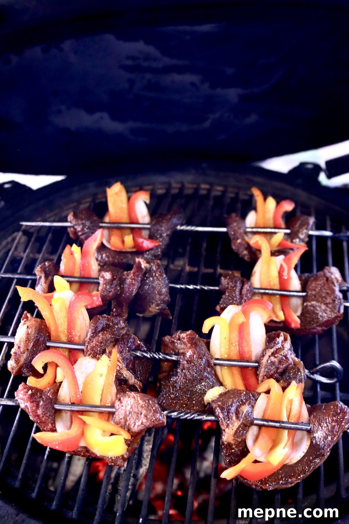 marinated steak skewers with peppers and onions on grill.