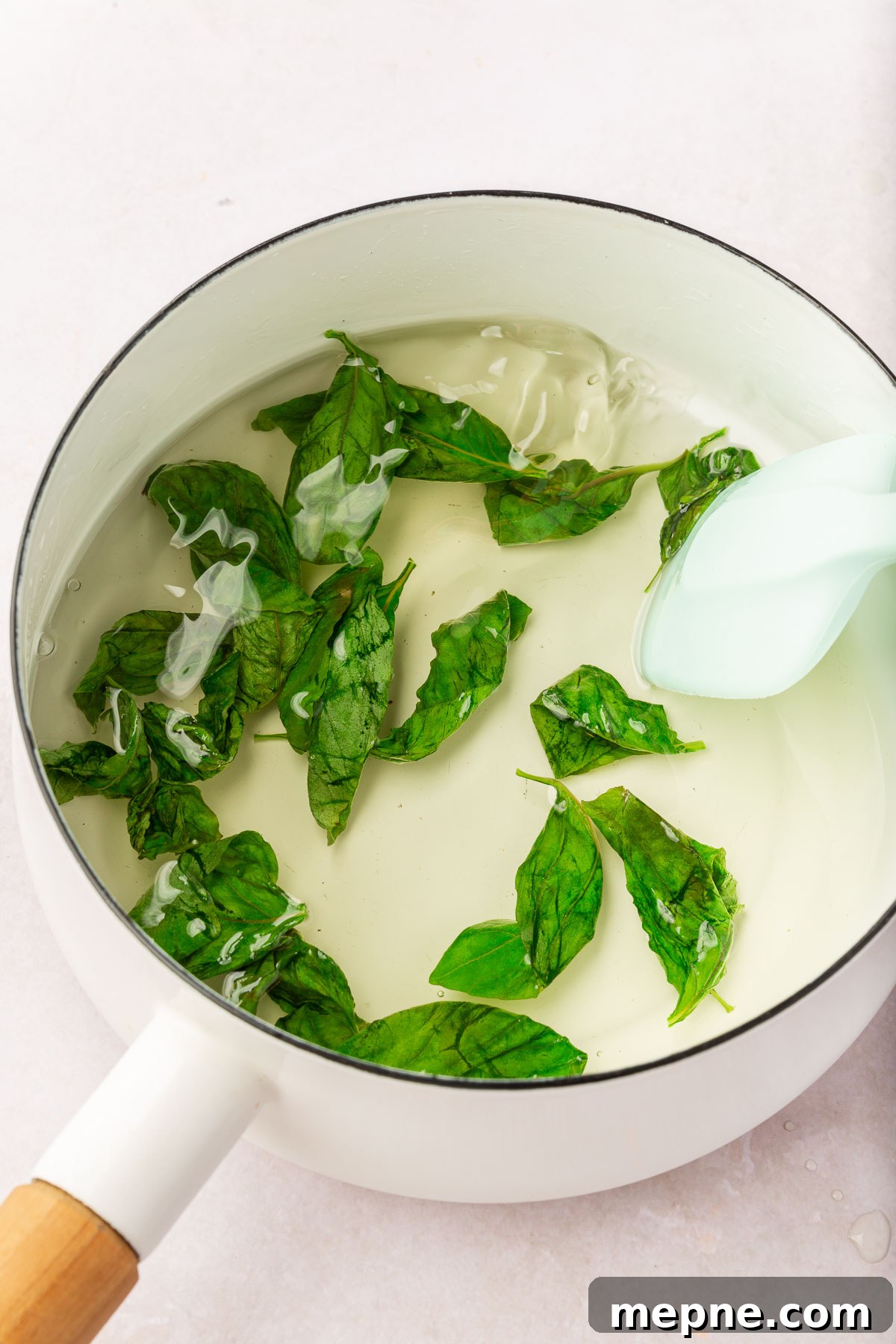 Fresh Basil Lemonade Recipe 4 A saucepan of basil simple syrup being stirred by a silicone spatula.