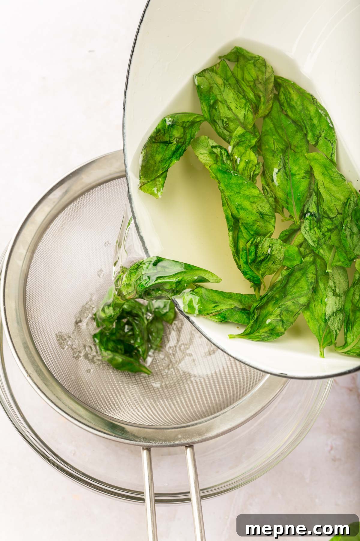 Fresh Basil Lemonade Recipe 5 A saucepan pouring basil simple syrup into a wire mesh strainer to strain out the fresh basil.