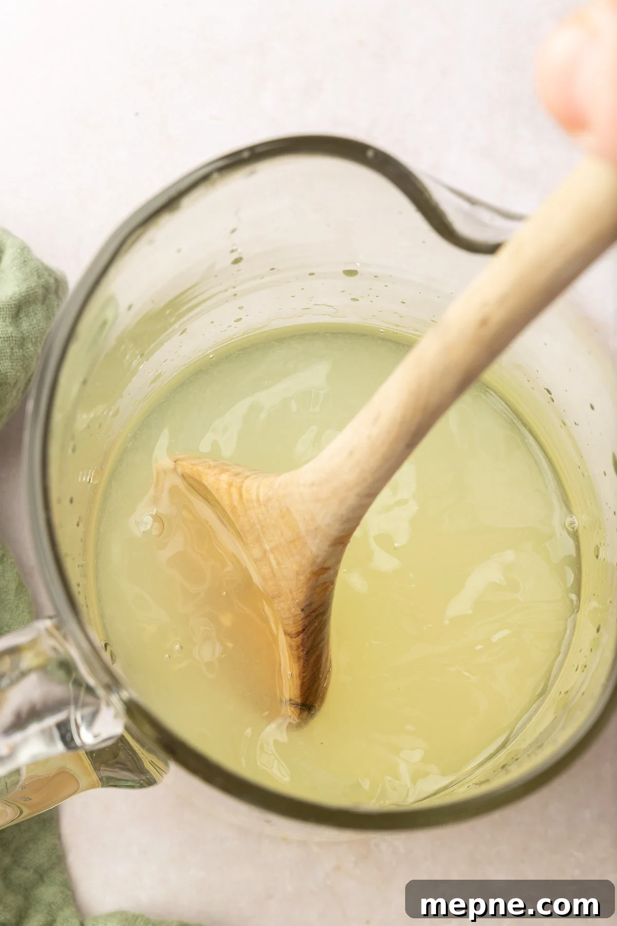 Fresh Basil Lemonade Recipe 8 A wooden spoon stirring lemonade in a glass pitcher.