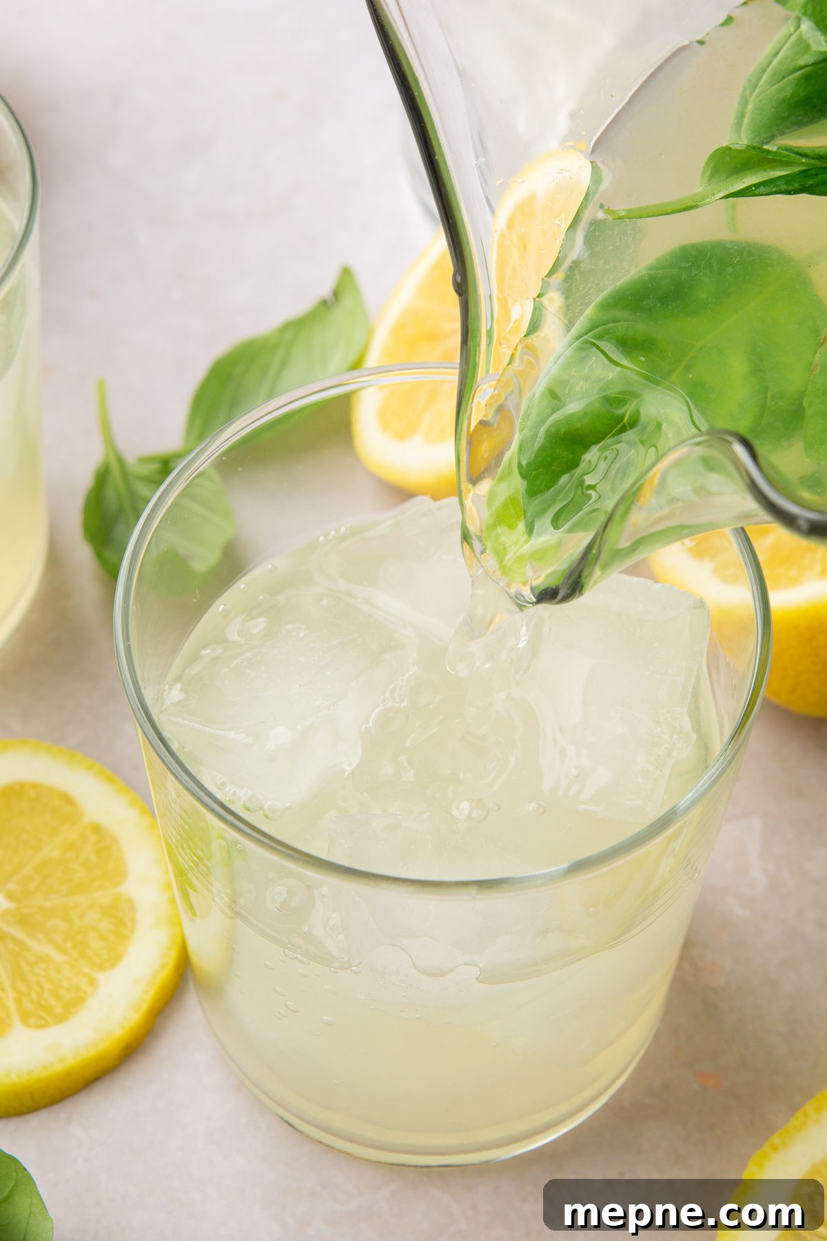 Fresh Basil Lemonade Recipe 9 A pitcher pouring basil lemonade into a glass filled with ice.