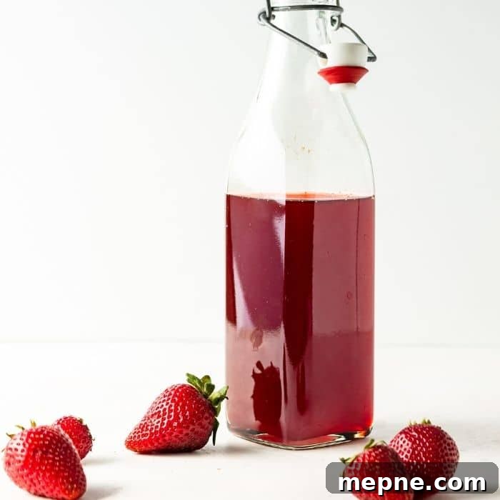 Homemade Strawberry Syrup for Cocktails and Mocktails 8 glass jar of fruit syrup on counter with berries in front