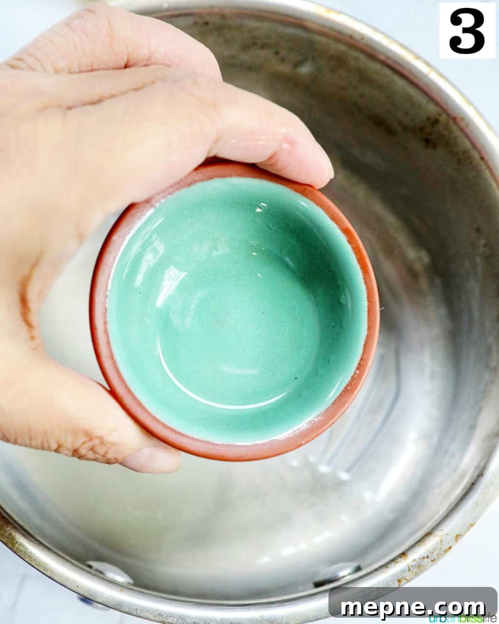 White Chocolate Peppermint Mocha Recipe 8 hand holding a small bowl of peppermint extract over a saucepan.