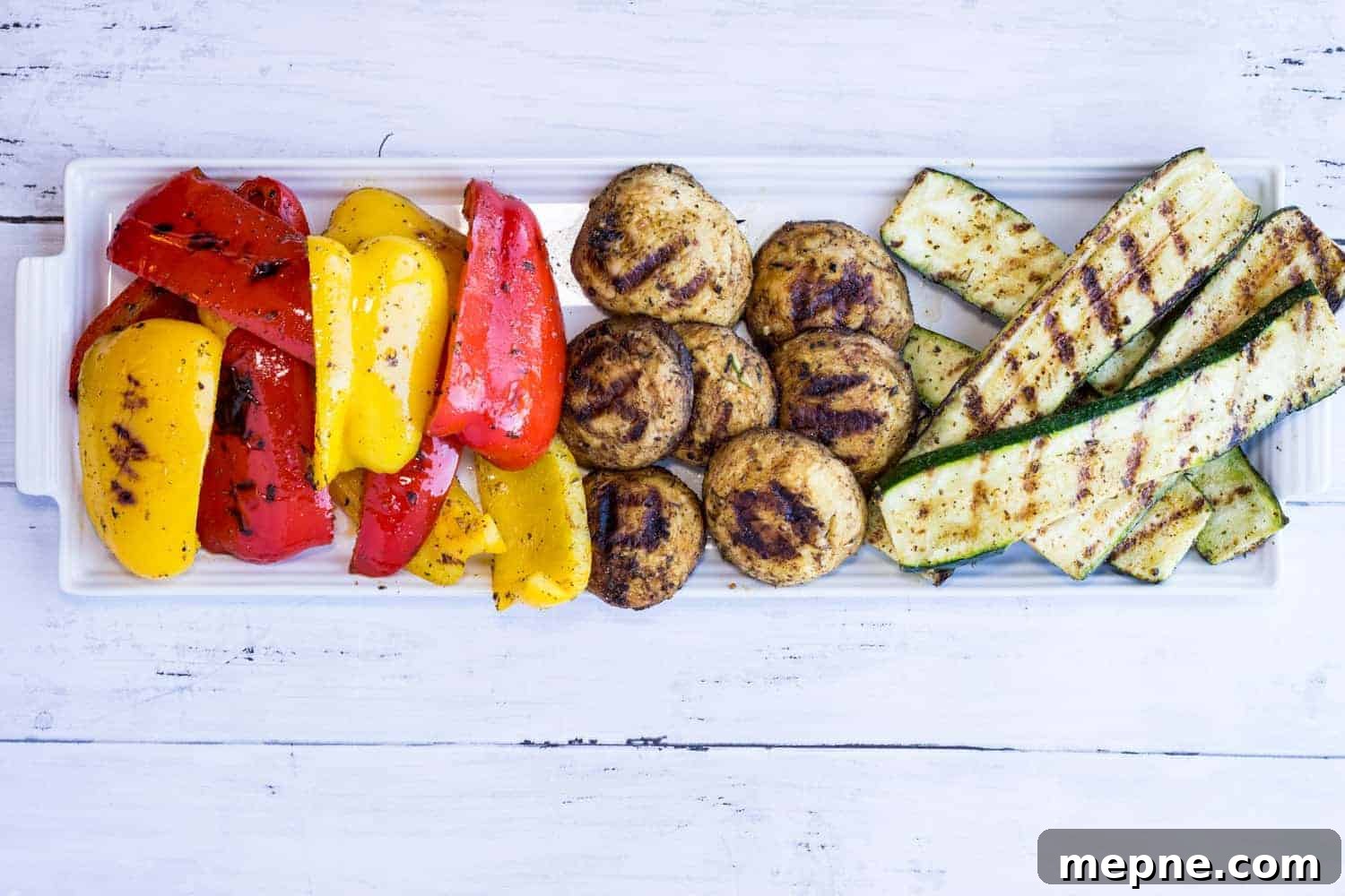 33 BBQ Recipes That Turn Budget Cuts Into Gourmet Meals 15 Grilled vegetables on a rectangular white platter, including red and yellow bell peppers, mushrooms, and zucchini slices.