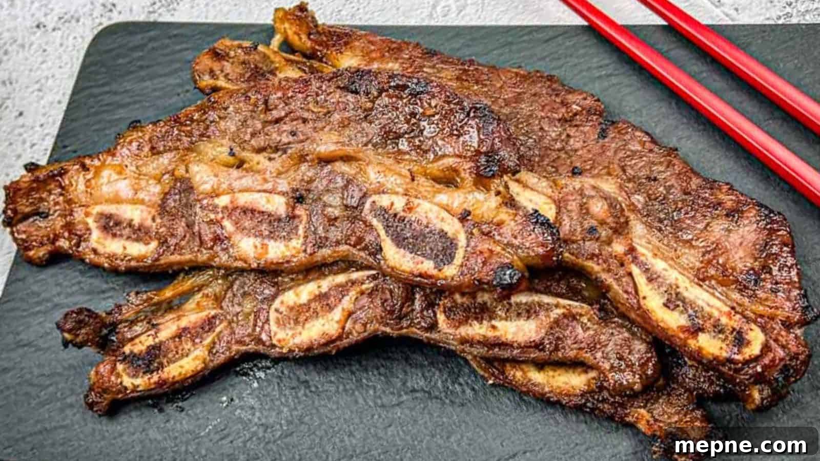 33 BBQ Recipes That Turn Budget Cuts Into Gourmet Meals 17 Korean Galbi Ribs on a slate platter with red chopsticks beside them.