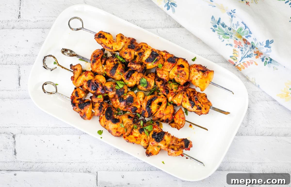 33 BBQ Recipes That Turn Budget Cuts Into Gourmet Meals 20 A rectangular white plate with four Sweet & Spicy Grilled Harissa-Honey Chicken Skewers garnished with chopped herbs.