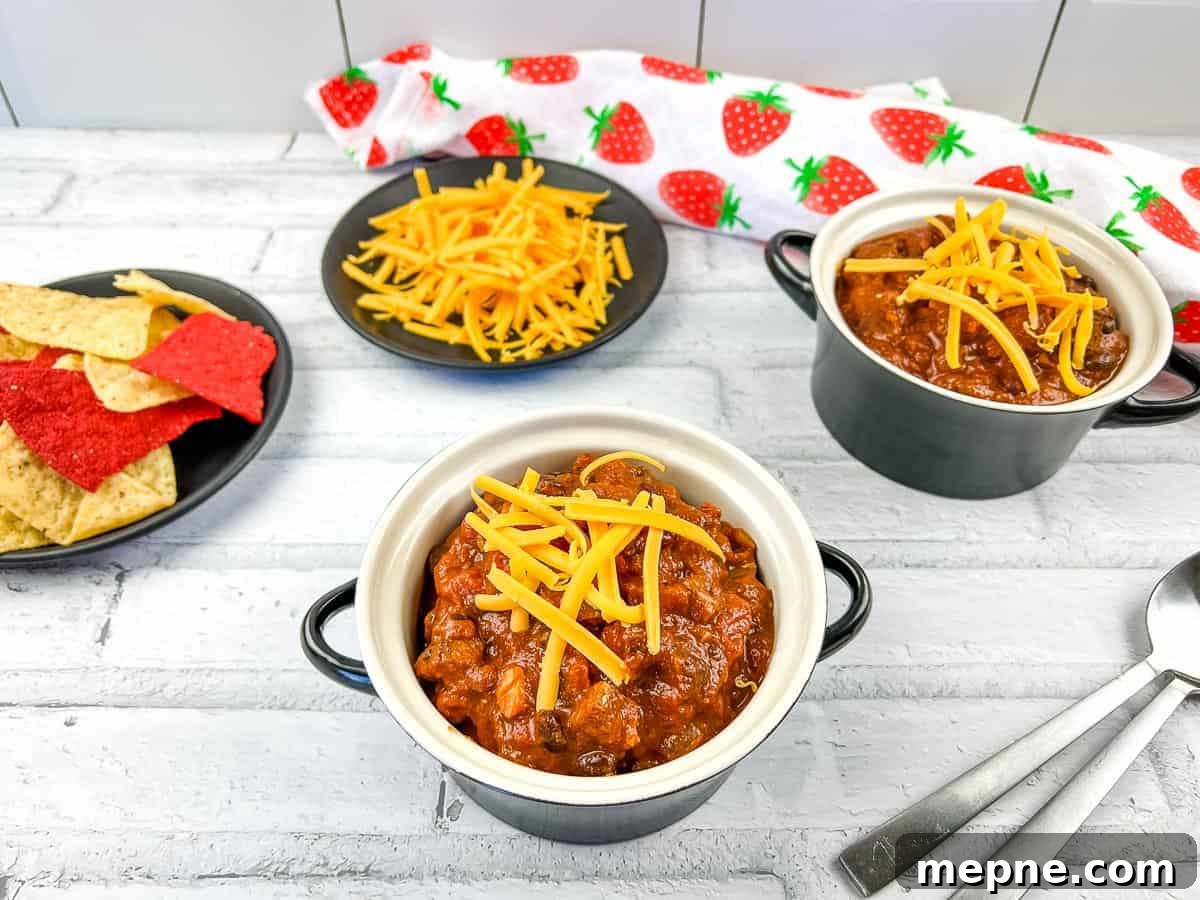 33 BBQ Recipes That Turn Budget Cuts Into Gourmet Meals 21 Smoked brisket chili served in two black bowls topped with sour cream, surrounded by fresh tomatoes, shredded cheese, crusty bread, and two spoons on a gray surface.