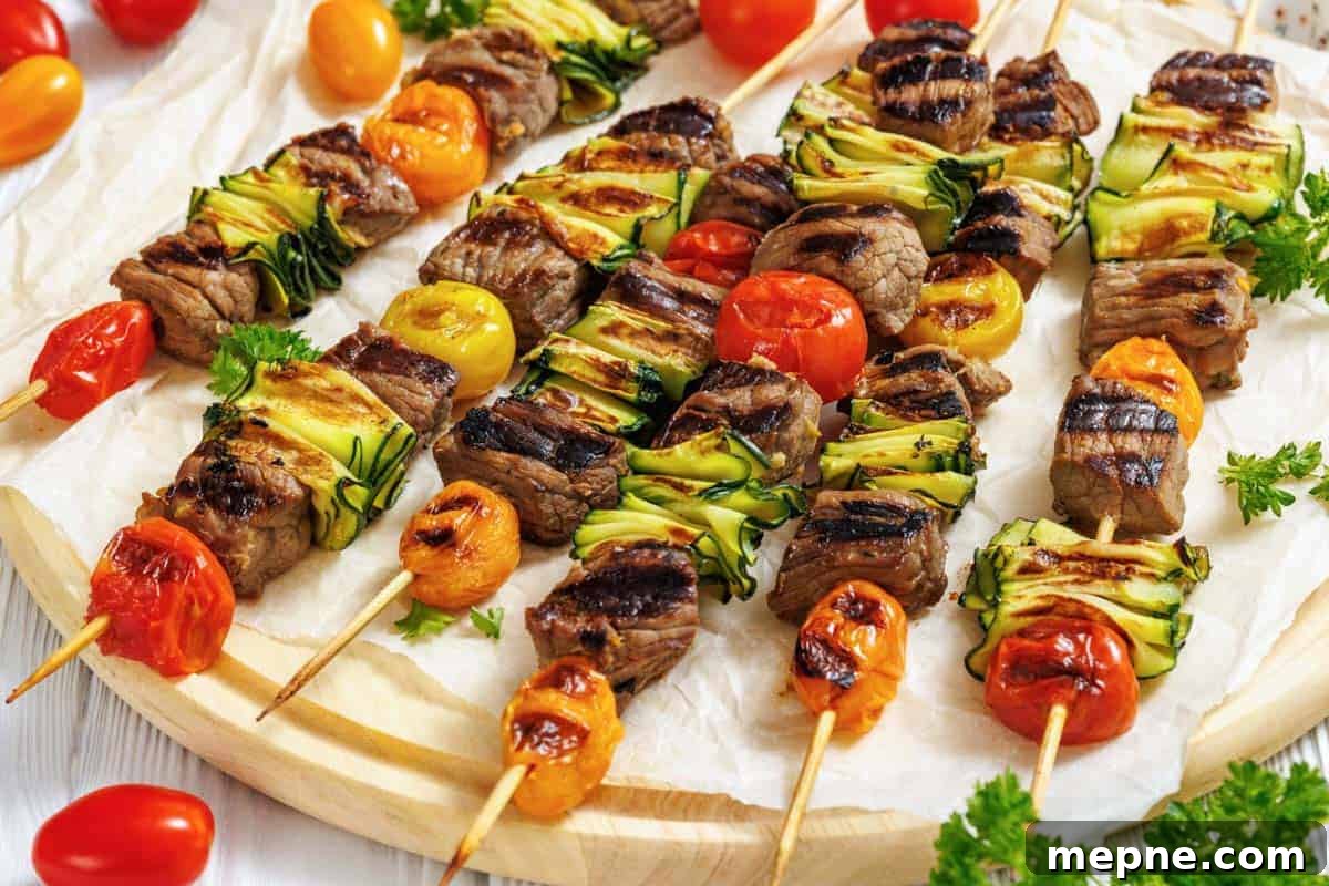 33 BBQ Recipes That Turn Budget Cuts Into Gourmet Meals 27 A wooden round serving board is covered with white parchment paper, displaying numerous grilled steak and veggie skewers arranged horizontally across it.