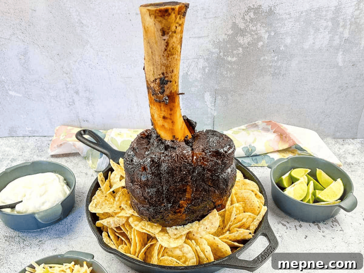 33 BBQ Recipes That Turn Budget Cuts Into Gourmet Meals 29 A large roasted meat shank on a bone, displayed upright in a skillet surrounded by nachos, with bowls of lime wedges and sauce nearby.