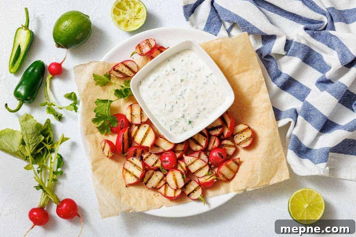 33 BBQ Recipes That Turn Budget Cuts Into Gourmet Meals 4 A plate with grilled radishes, a bowl of creamy dipping sauce, lime halves, jalapeño, and a striped cloth on a white surface.