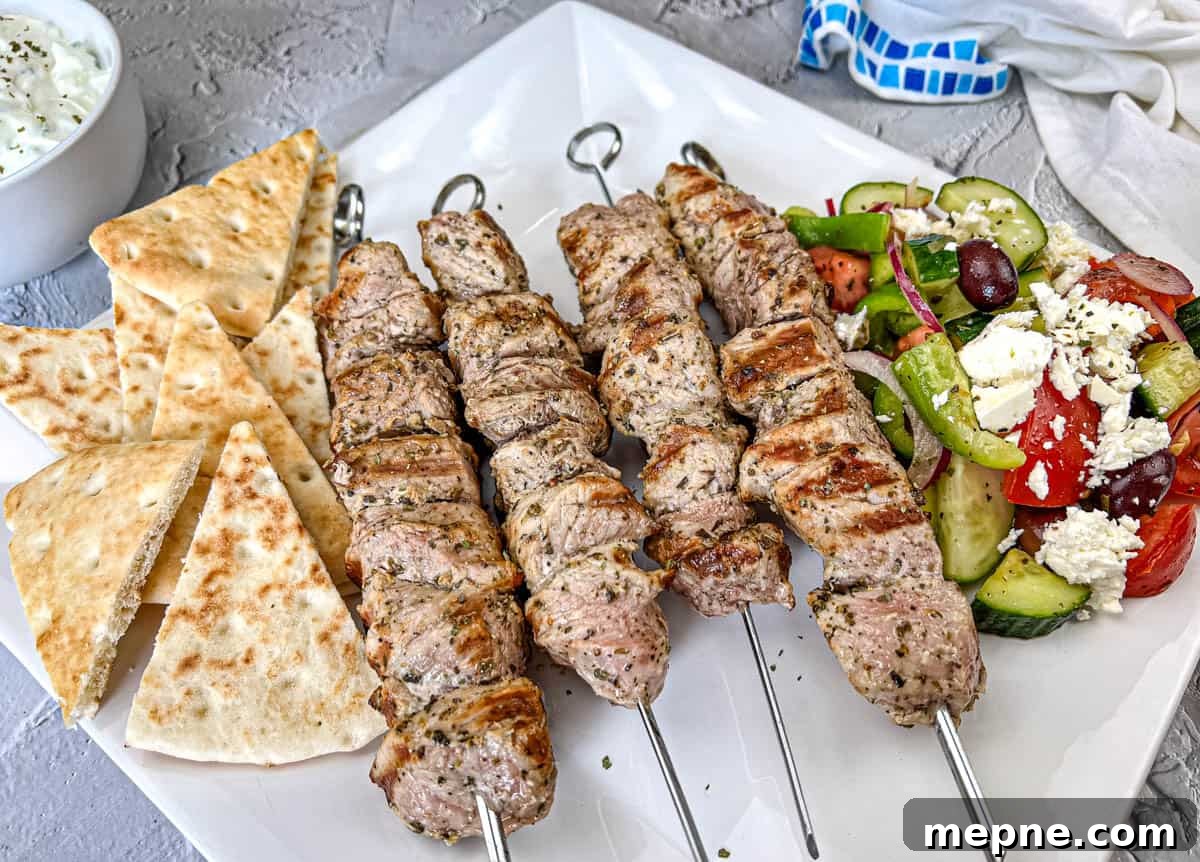 33 BBQ Recipes That Turn Budget Cuts Into Gourmet Meals 5 Ninja Woodfire Pork Souvlaki with Horiatiki Salad and pita bread on a white plate.