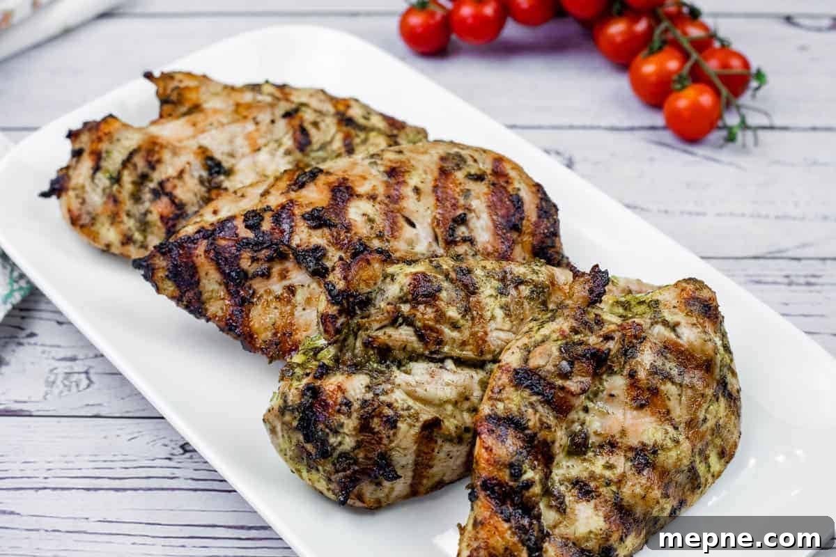 33 BBQ Recipes That Turn Budget Cuts Into Gourmet Meals 7 Grilled lime-garlic chicken breasts with visible char marks on a white rectangular plate, with vine tomatoes in the background.